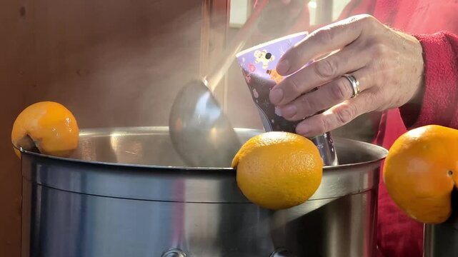 Hand pouring a traditional mulled wine to the glass from a large pot with rising steam. Strasbourg Cristmas market cozy setting.