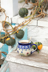 A beautiful ceramic tea cup on the stairs of the old veranda with small autumn pumpkins. Selective focus.