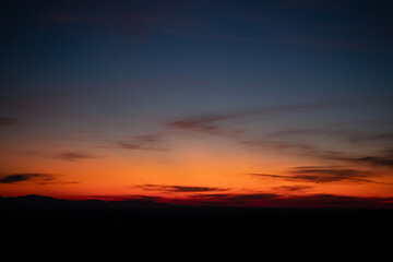 Twilight sunset with deep orange and blue hues over the horizon. Silhouette of mountains. Fading sunlight. Peaceful, dreamy atmosphere, tranquility, transition, natural beauty, quiet magic of dusk.