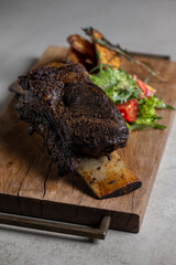 roasted veal rib with baked potatoes and vegetables on a wooden board