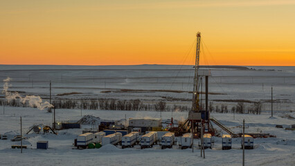 Expansive winter vista of industrial drilling rig complex amid snow-covered plain, featuring crew...