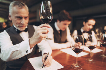 Confident sommelier tasting wine in restaurant. Tasting specialist makes notes.