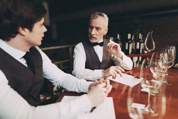 Confident young and old sommeliers discuss quality of wine drink in restaurant.