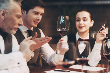 Three sommeliers assess taste and color qualities of wine when examining glass in restaurant.