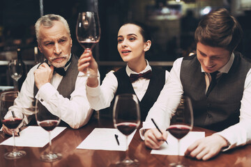 Beautiful female sommelier is holding glass of wine and tasting sediments.