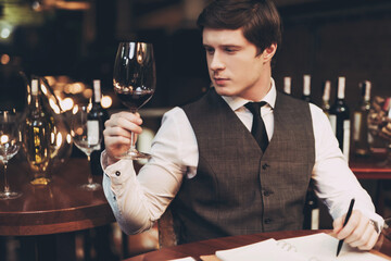 Young confident sommelier makes notes in notebook, tasting wine in restaurant. Wine tasting.