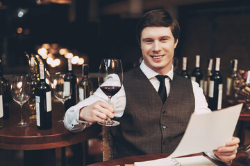 Young confident sommelier makes notes in notebook, tasting wine in restaurant. Wine tasting.