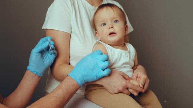 A caregiver holds a baby during a vaccination appointment at a health clinic, as a healthcare professional prepares to administer the inoculation. This crucial health activity supports child health