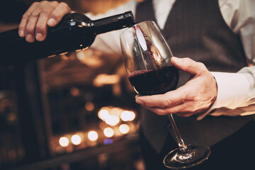 Close up. Elegant waiter pours red wine from bottle into glass in restaurant. Sommelier tasting wine in restaurant.
