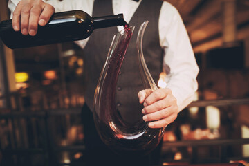 Close up. Elegant waiter pours red wine from bottle into decanter in restaurant. Sommelier tasting wine in restaurant.
