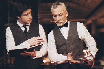 Two experienced sommeliers taste wine. Sommelier pours red wine from decanter into glass.
