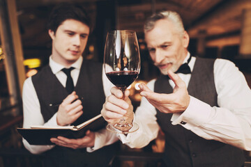 Two experienced sommeliers taste red wine and make wine list in restaurant.