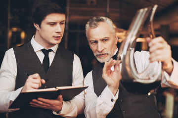 Experienced elegant sommeliers looks at wine sediment in decanter. Wine degustation. Sommelier compose of wine list.

