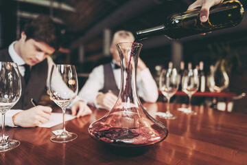 Experienced sommelier makes notes about taste qualities of wine drink sitting in restaurant.