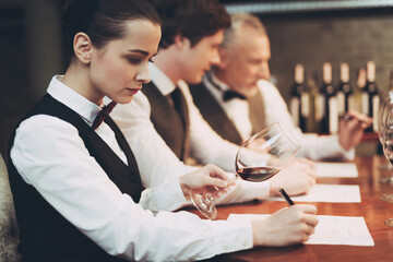 Female sommelier tasting red wine and making notes at degustation card.