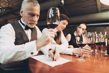 Confident sommelier tasting wine in restaurant. Tasting specialist makes notes.