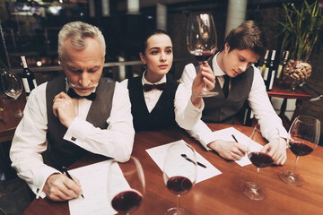 Beautiful female sommelier is holding glass of wine and tasting sediments. Confident sommelier tasting wine in restaurant.
