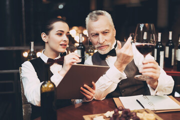 Experienced sommelier tells young girl about specifics of taste of red wine in restaurant.