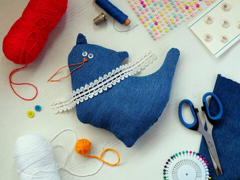 DIY Handmade Denim Cat Plush Toy with Sewing Supplies and Decorative Elements on Craft Table