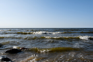 Small foaming sea waves roll in frontally. Blue sky on a sunny summer evening. Light breeze on the seascape
