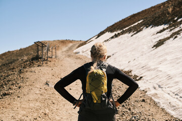 Woman hiker pauses on mountain trail, backpack on, gazing at snowy peak ahead.  Stunning landscape...