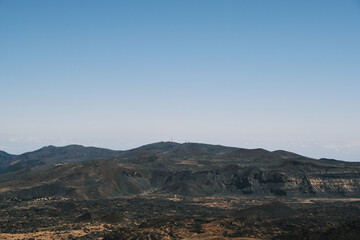 Panoramic view of a volcanic landscape under a clear blue sky. Rugged terrain and distant mountains create a dramatic, serene scene. Ideal for travel, nature, and adventure projects.