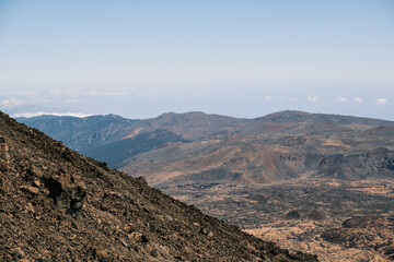 Panoramic view of a volcanic landscape. Rugged, dark brown mountains under a clear blue sky. Ideal for travel, nature, and geology projects.