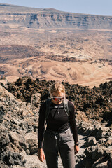 A hiker with a backpack pauses on a rocky mountain path, taking in the breathtaking volcanic...