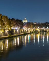Reflections in the Tiber River with Vatican City and a historic arched bridge in the background at night. Ponte Umberto I