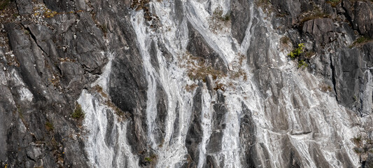 A rocky mountainside with white trails and depressions washed out by rain