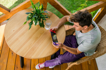 Young man playing video game drinking water at terrace in summer day. Technology and game addiction concept