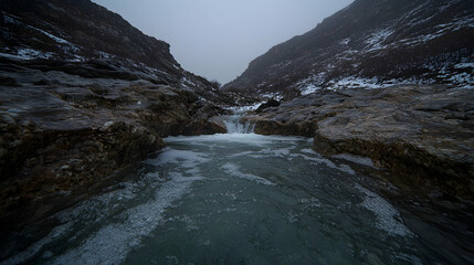 Mountain stream flows through rocky gorge, snowy peaks background, nature scene