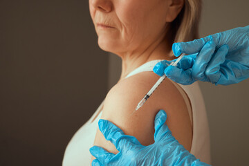 A healthcare worker in gloves administers a vaccine to a senior woman in a bright indoor space. The...