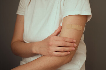 A person with a bandage on their arm after receiving a vaccination sits against a neutral backdrop....