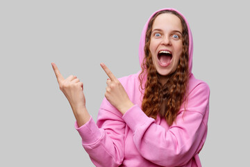 A young woman wearing a bright pink hoodie shows enthusiasm by pointing in two separate directions....