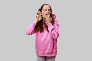 A young woman wearing a pink hoodie expresses surprise and curiosity, covering her mouth with one...