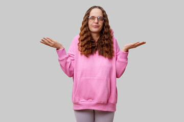 A young woman wearing a pink hoodie stands in front of a gray backdrop, raising her hands in a...