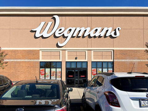 A white car is parked in front of a Wegmans store