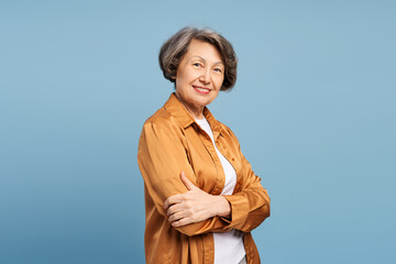 Smiling senior woman with crossed arms on blue background