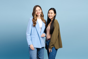 Two young women smiling and posing together on blue background