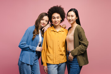 Three young women embracing diversity and friendship on pink background