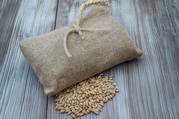 Rustic Harvest: A burlap sack filled to the brim with golden grains sits beside a scattering of loose kernels on a weathered wooden surface, symbolizing the bounty of the harvest.