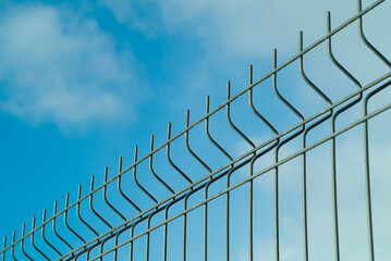 green fence made of 3d mesh panels close-up on blue sky background