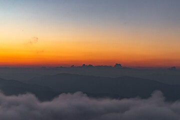 Obraz premium clouds spread between mountain ranges after sunset, the sky burns orange