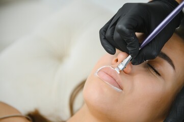 Woman beautician prepares the patient, a young woman, for permanent makeup lips, drawing the...