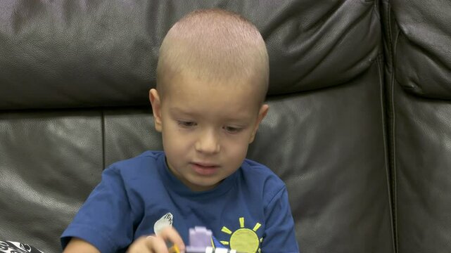 Child playing with new toy sitting on sofa at home. Concentrated face of little boy holding transformer robot toy. Three year old child examining new toy comments on his actions.