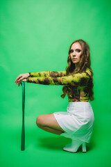 Young woman sitting with a tennis racket on a green background, studio shot