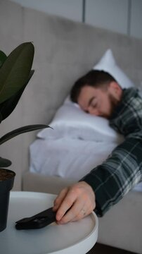 Young man ignores the ringing alarm clock on his phone in the morning and goes back to sleep