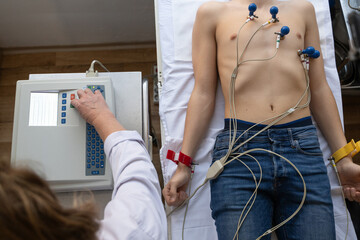 A female doctor performs an ECG on a young man in a hospital room, carefully monitoring his heart...