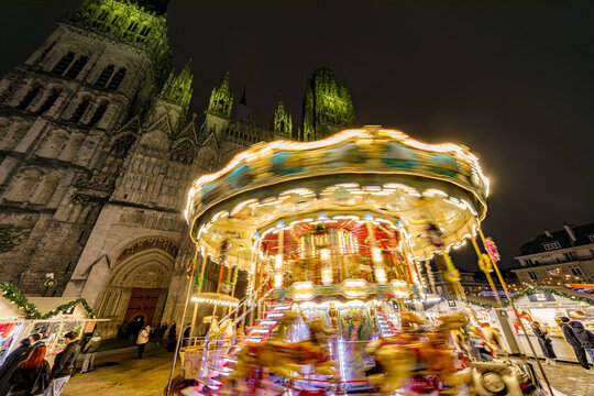 ROUEN, NORMANDY, FRANCE - 2025: carousel at Christmas Market, chalets with delicatessen shops, illuminated Notre Dame Cathedral, cobbled pedestrian street in historic center